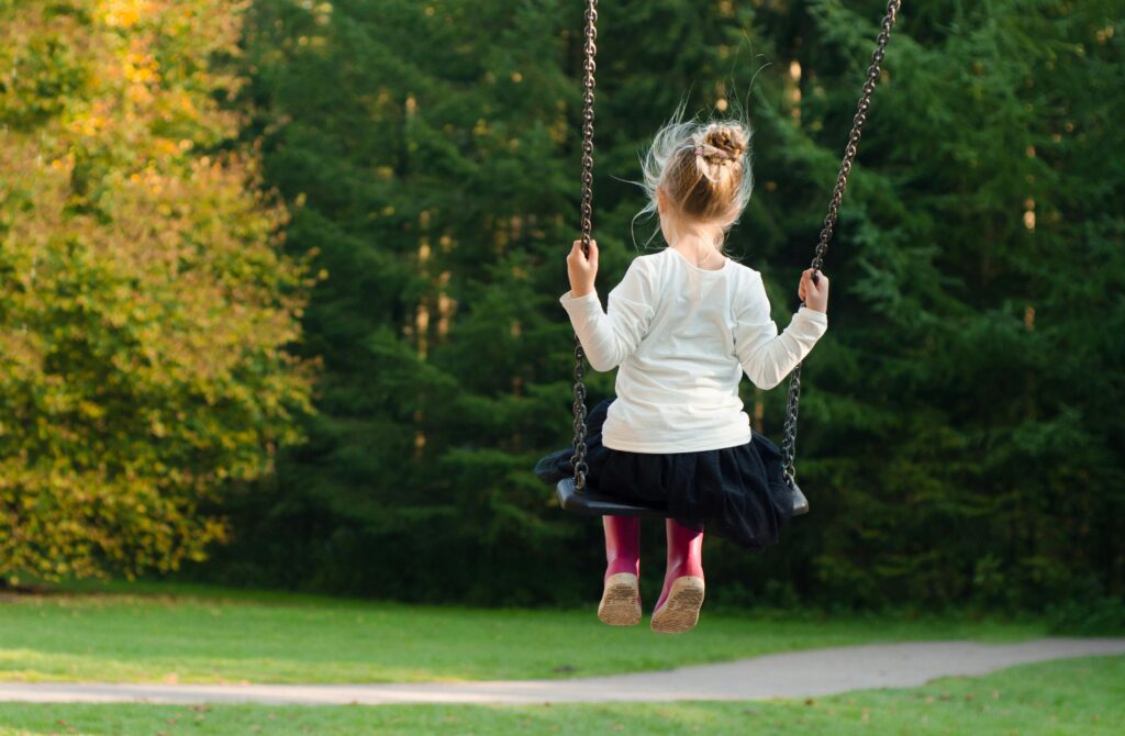 Young girl swinging in the park, surrounded by lush greenery on a sunny day.