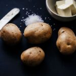 Artistic still life showcasing potatoes, butter, and salt on a dark background.